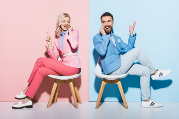 smiling woman and handsome man talking on smartphones on pink and blue background
