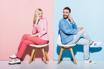 smiling woman and handsome man talking on smartphones on pink and blue background