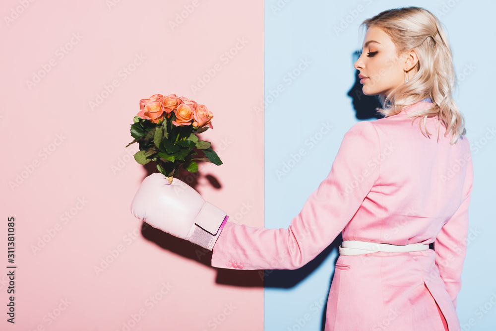 Wall mural attractive woman in boxing glove holding bouquet on pink and blue background