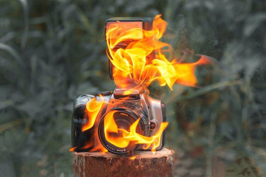 on the wooden stump there is a digital SLR camera and burns with flame
