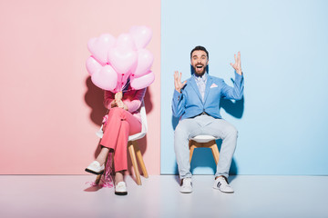 Fototapeta na wymiar woman holding balloons and shocked man with outstretched hands on pink and blue background