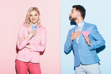 smiling woman and handsome man with heart-shaped card on pink and blue background