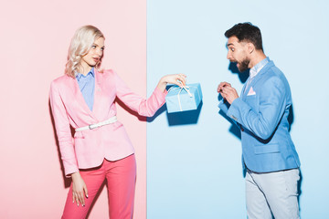 attractive woman giving present to shocked man on pink and blue background