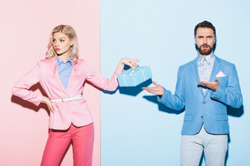 sad woman holding gift and shocked man pointing with hands on pink and blue background