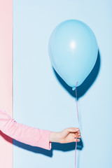 cropped view of woman holding balloon on pink and blue background