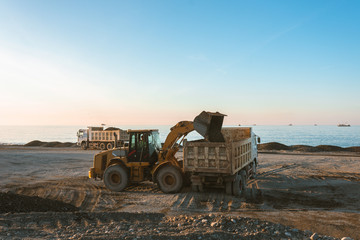 Excavator loads the excavation onto a truck (hydraulic)are heavy construction equipment consisting of an arrow,a bucket and a cabin on a rotating platform.On the beach with the sea and the setting sun