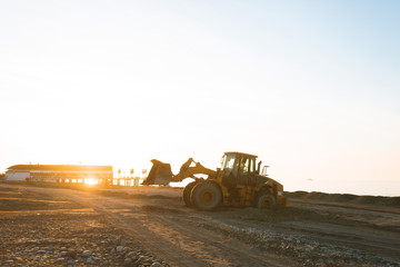 Excavator loads the excavation onto a truck (hydraulic)are heavy construction equipment consisting of an arrow,a bucket and a cabin on a rotating platform.On the beach with the sea and the setting sun