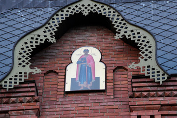 On the brick facade of the temple is the face of St. Alexander 3. The icon hangs on a brick red wall.