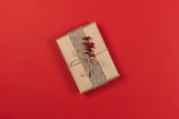 Craft gift box with branch of red berries on red background. Holiday eco-friendly concept.