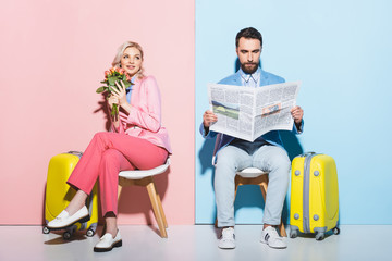 smiling woman holding bouquet and man reading newspaper on pink and blue background