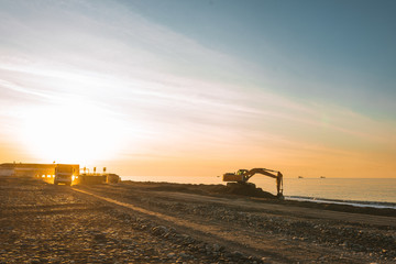 Fototapeta na wymiar Excavator loads the excavation onto a truck (hydraulic)are heavy construction equipment consisting of an arrow,a bucket and a cabin on a rotating platform.On the beach with the sea and the setting sun