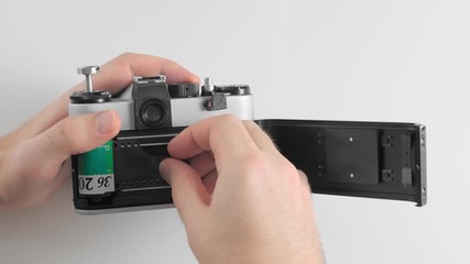 An unrecognized man inserts green film into the body of an old vintage retro camera.