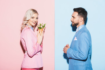 side view of smiling woman with bouquet and handsome man on pink and blue background