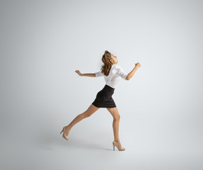 Fototapeta na wymiar Hurrying up to new goals. Woman in office clothes running on grey studio background. Businesswoman training in motion, action. Unusual look for sport, new activity. Sport, healthy lifestyle.