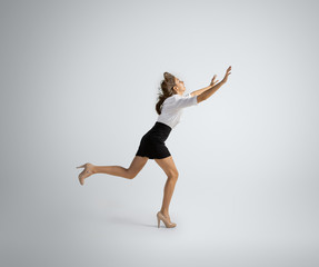 Obraz premium Hurrying up to new goals. Woman in office clothes running on grey studio background. Businesswoman training in motion, action. Unusual look for sport, new activity. Sport, healthy lifestyle.