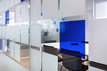Glass wall with decorative squares separates rooms in office. Empty conversation room with table and chairs in modern office interior.