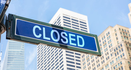 Closed street sign, blue color. Highrise buildings and blue sky background,