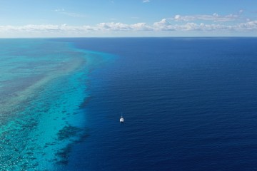 Catamaran on ocean with deep blue sea to one side and turquoise Caribbean coral sea to other side 