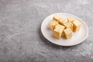 traditional indian candy soan papdi in white plate with almond and pistache on a gray concrete background. side view