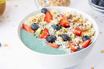 Detox breakfast smoothie bowl with spirulina, blueberry, strawberry, granola, kiwi, banana, coconut and chia seeds. Spirulina smoothie with berries and fruits in bowl.  