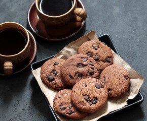 Chocolate chip cookies with dark chocolate slices with milk and coffee on a dark gray background