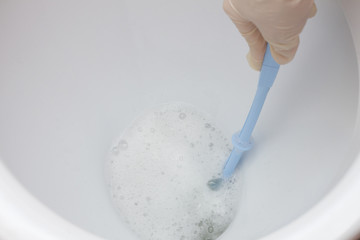 Female hands in gloves wash and disinfect a white toilet with a brush and cleaning agent