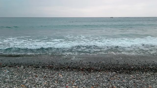 View from the stony beach of the sea with seagulls and boat. The waves coming