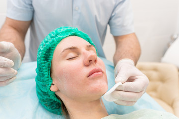 Cosmetologist applying cream on female face in cosmetology salon.