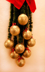 Holidays wreath made of green fir branches with Christmas baubles ornaments. Twigs of pine, golden balls and red bows as Christmas decorations on wall background of apartment. Celebration concept.