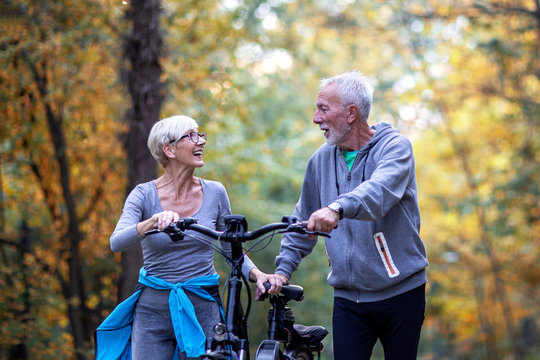 Mature couple woman and man with bicycle walking in the park and talk