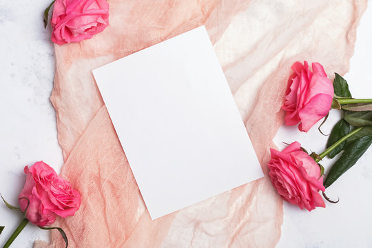 Top view of blank paper card lying on the pastel color cloth on the table with pink roses.