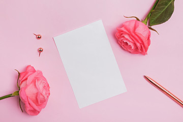 Blank paper card lying on the pink table with roses and gold color stationery.