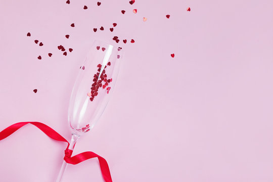 Sparkling wine glass with snal red star shaped confetti on pink background,
