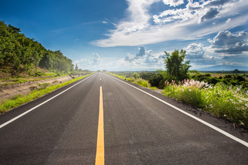 Asphalt road through the green field and clouds on blue sky in summer day. Beautiful grassland road in Thailand.Highland road.