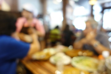 blurred image of group of people of enjoy talking and eating some food with their family on table in restaurant. vintage tone and light effect. Abstract restaurant interior for background