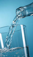 Nalewanie wody z butelki do szklanki na niebieskim tle