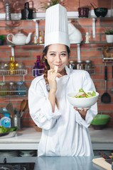 Smiling young asia woman chef cook in white uniform standing at the kitchen