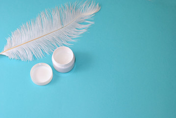 Big white feather and white and cream jar with free empty copy space. Skin care concept