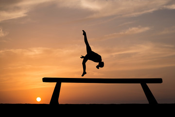 silhouette of female gymnast on balance beam in sunset