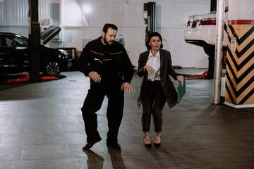 Good looking manager woman in a suit and the mechanic man attractive look dancing in a garage after they finished the work day