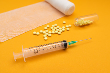 Syringe with pills for injection and vaccination on yellow background with bandage, concept of...