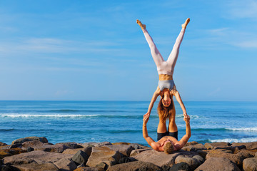Fit young couple doing acro yoga at spa retreat on sea beach. Active woman on partner feet,...