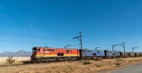 Hermon, South Africa. December 2019. Freight trains hauling wagons through countryside with a mountains backdrop.