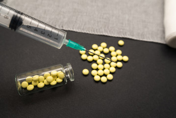 Syringe with pills for injection and vaccination on black background with bandage, concept of medecine