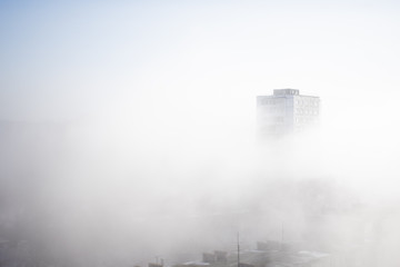 Fototapeta premium White clouds of fog envelop buildings at residential district. Urban panorama