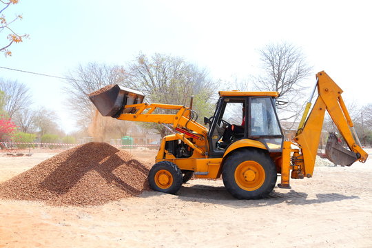 A backhoe dumping crushed stone.This is a type of excavating equipment consisting of a tractor-like unit fitted with a loader-style shovel/bucket on the front and a backhoe on the back.