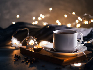 Home atmosphere of Christmas and holiday. A white Cup of coffee on an old book , a garland in the shape of a Christmas tree and a warm scarf