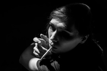 Beautiful girl smokes a cigarette in a dark building. Black and white photo