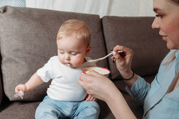 young mother feeds her daughter with a spoon of fruit puree