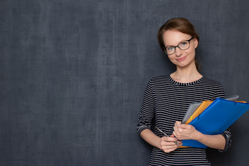Portrait of happy young woman smiling and holding folders and pen